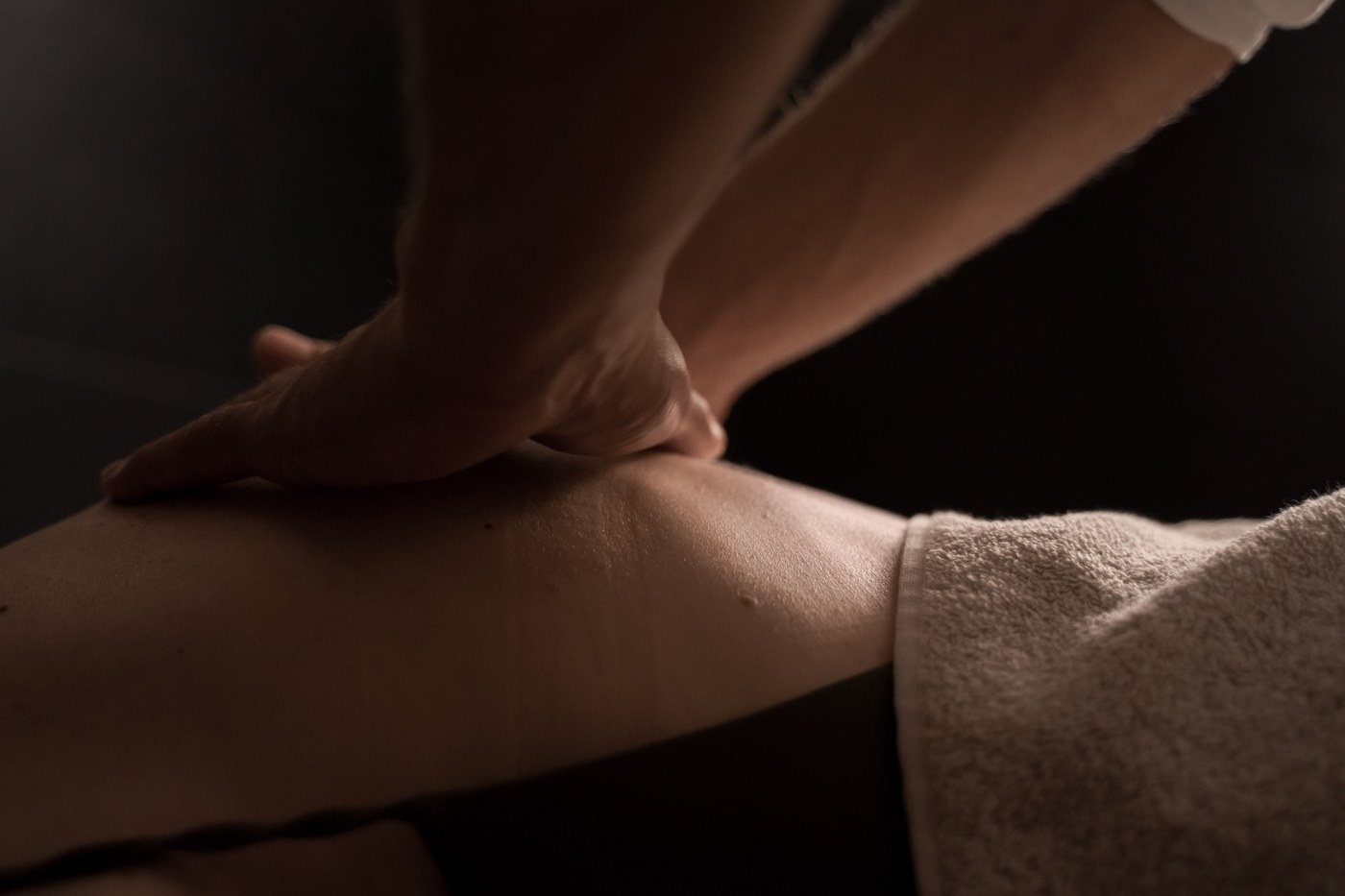 Hender som masserer et ben i dempet lys
